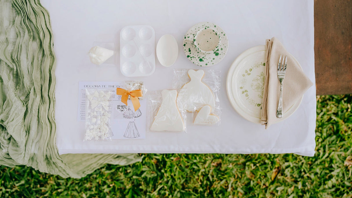 Table setting with plates, cutlery, and DIY cookie items on a white cloth over grass.