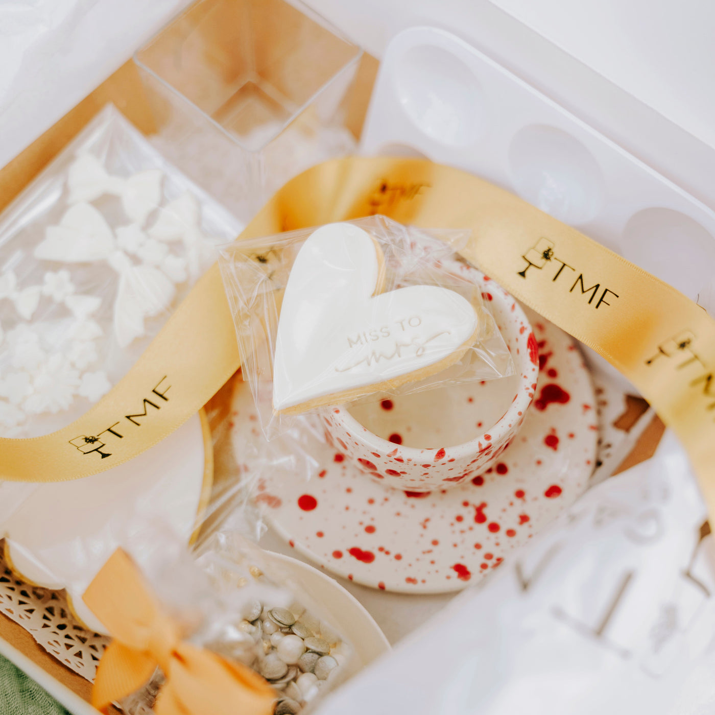 Heart-shaped white cookie in a decorative box with gold TMF ribbon