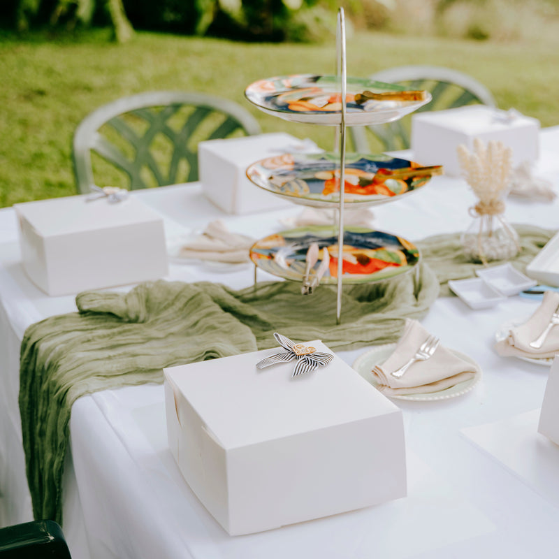 Outdoor setting with a table set for a DIY Cookie celebration, featuring a three-tiered serving tray with food.