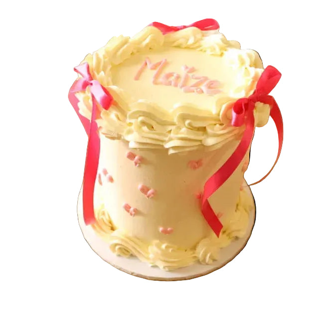 Decorative cake with pink ribbons and 'Maitre' text on a wooden surface with flowers.