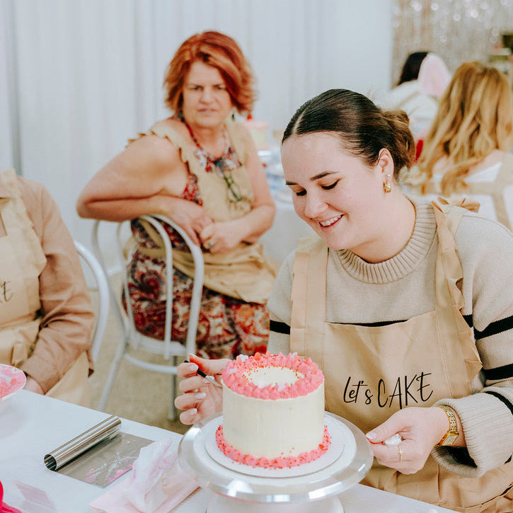 Woman in a cake decorating class with a small cake on a table.