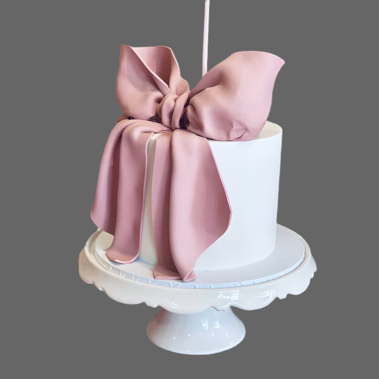 A Fondant Bow Cake with a large pink bow on top, presented on a white plate against a black background.