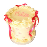 Decorative cake with pink ribbons and 'Maize' written on it, placed on a wooden table.