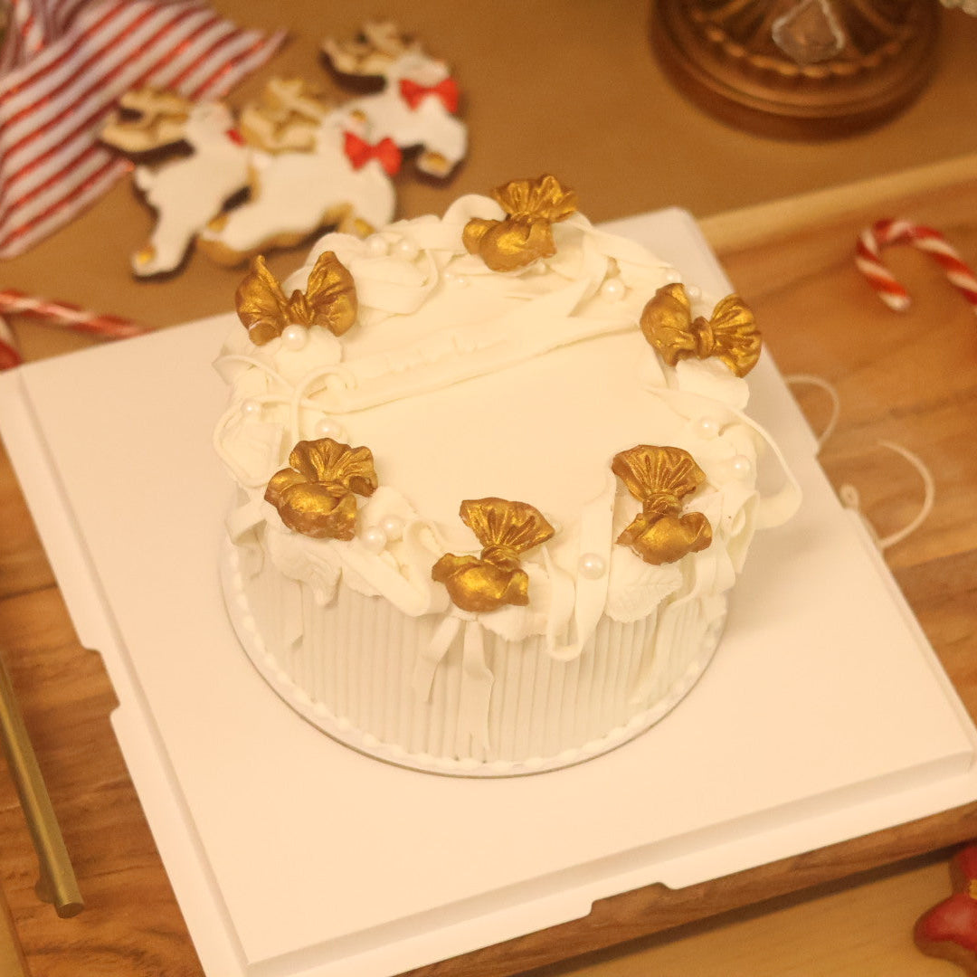 White cake with gold decorations on a wooden table with Christmas-themed decor.