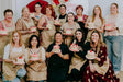 Group of women posing with decorated cakes in a room with a 'Cake & Sh...' sign.