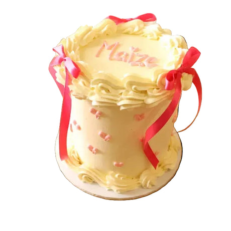 Decorative cake with pink ribbons and 'Maitre' text on a wooden surface with flowers.