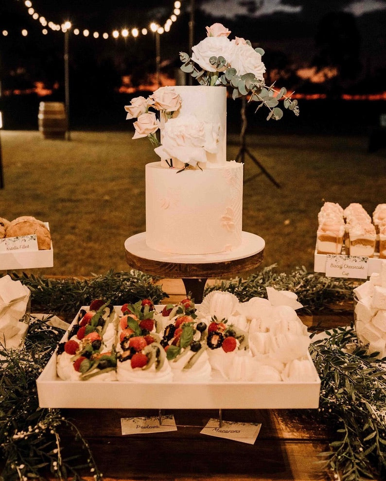 elegant white wedding cake on a stand, accompanied by desserts and sweet treats
