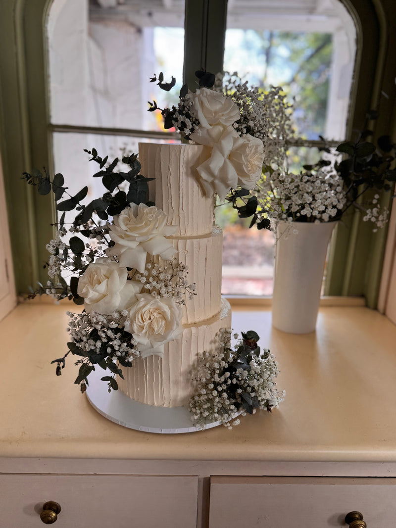 white wedding cake with florals, sitting on a dresser in front of a window